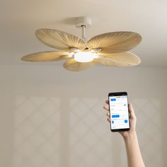 a person holding up a cell phone in front of a ceiling fan with lights on it