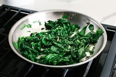 a pan filled with spinach on top of an oven burner next to a stove