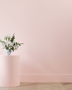 a white vase with flowers in it on a wooden floor next to a pink wall