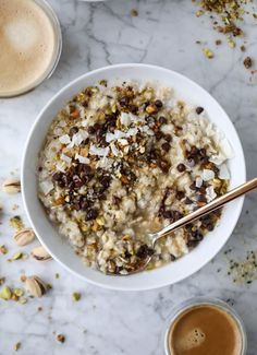 a bowl of oatmeal with nuts and seeds next to two cups of coffee