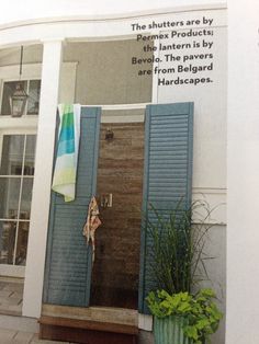 an open door with blue shutters and potted plants in front of it on the side of a building