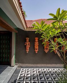 three wooden statues on the side of a building next to a plant and potted tree