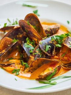 a white plate topped with mussels covered in sauce and garnished with parsley