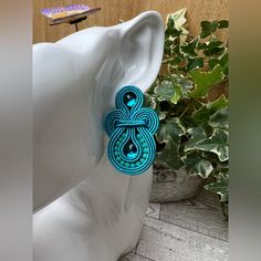 a pair of blue earrings sitting on top of a white vase next to a plant