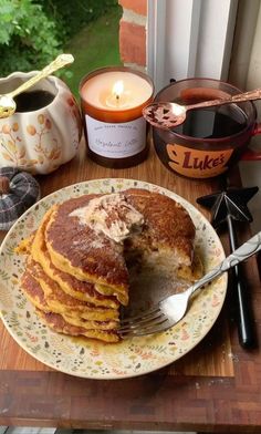 a stack of pancakes sitting on top of a plate next to a cup and candle