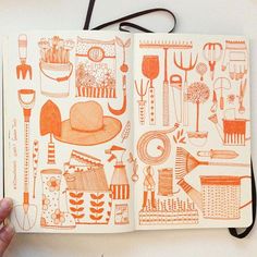 a hand holding an open notebook with orange doodles on the pages and utensils