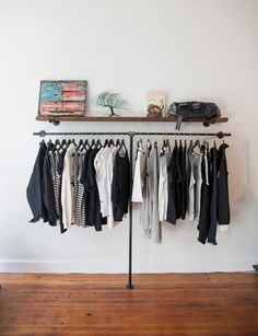 a rack with clothes hanging on it in front of a white wall and wooden floor