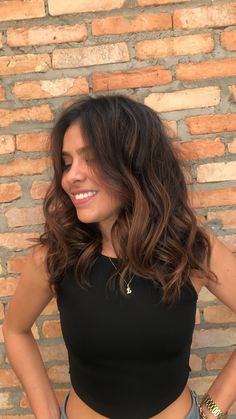 a woman standing in front of a brick wall with her hands on her hips and smiling