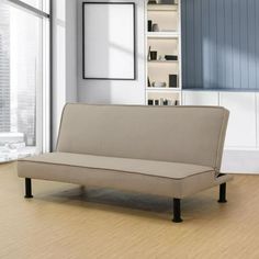 a couch sitting in front of a window on top of a hard wood floor next to a book shelf