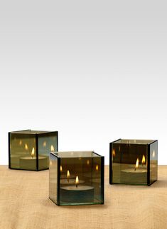 three glass cubes with lit candles in them sitting on the ground next to each other