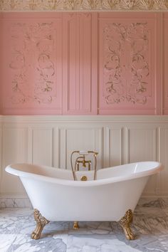 a bathtub in a bathroom with pink walls and gold fixtures on the wall behind it