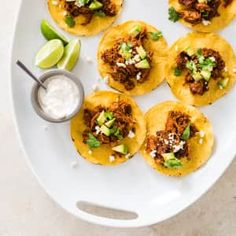 several tacos on a white plate with a small bowl of sour cream next to it