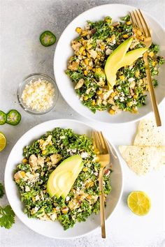 two white plates filled with salad and topped with avocado wedges next to lime slices