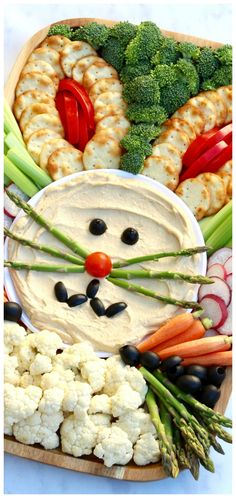 a platter filled with vegetables, crackers and a snowman face made out of cauliflower