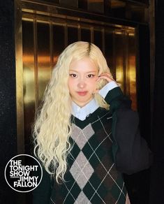 a woman with long blonde hair wearing a black and white sweater standing in front of an elevator