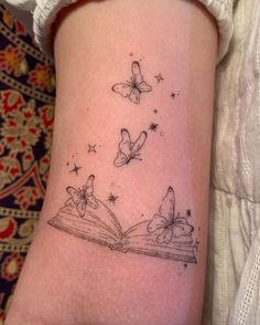 a woman's arm with butterflies flying over an open book on her left side