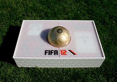 a golden soccer ball sitting on top of a white box in the middle of grass