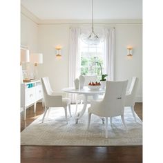 a white dining room table and chairs in front of a window with light coming through