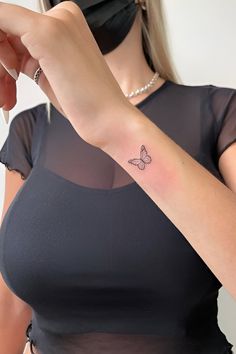 a woman with a small butterfly tattoo on her left arm, wearing a black top