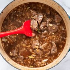 a pot full of stew with a red ladle in it on a marble counter top