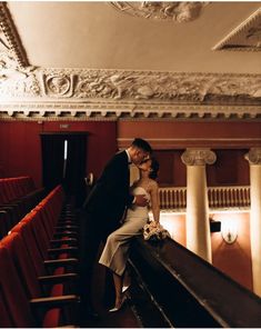 a bride and groom standing on the balcony of an old theater looking down at each other