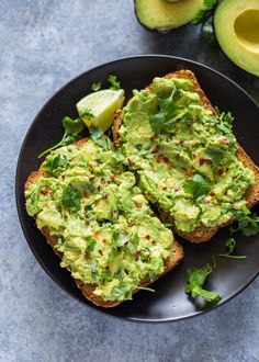 two pieces of bread with avocado on top and sliced limes in the background