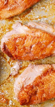 three pieces of meat cooking in oil on a stove top with seasoning sprinkles