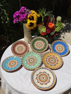 six plates on a table with flowers in the background