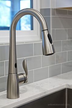 a stainless steel kitchen faucet and sink in a white tile backsplash