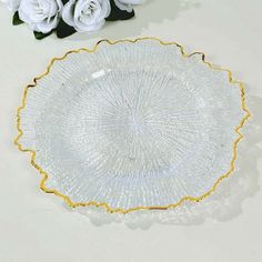 a glass plate sitting on top of a table next to white flowers and greenery