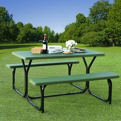 a picnic table with two benches and a bottle of wine on it in the grass