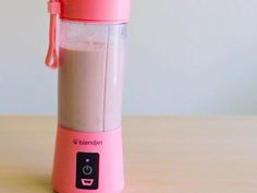 a pink blender sitting on top of a wooden table next to a white wall