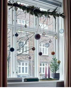 a window with ornaments hanging from it's side and a christmas tree in the corner