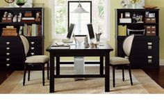 a desk with two chairs and a bookcase in front of a window that has books on it