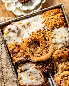 a pan filled with cinnamon rolls covered in icing next to pine cones and two forks