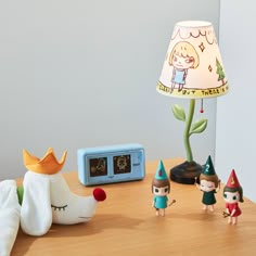 there is a lamp, figurines and an alarm clock on the wooden table