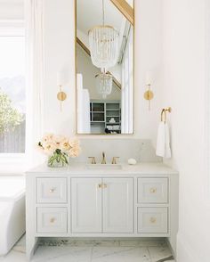 a white bathroom with a large mirror above the sink and flowers on the counter top