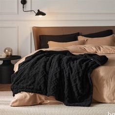 a bed with a black blanket on top of it next to a night stand and lamp