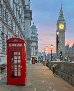 a red phone booth sitting on the side of a road next to a tall clock tower