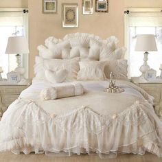 a bed with white ruffled bedspread and pillows in a room filled with pictures