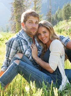 a man and woman are sitting in the grass with their arms around each other, smiling