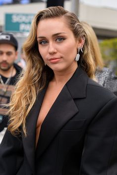 a woman in a black suit is posing for the camera with other people behind her