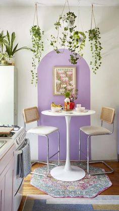 a small kitchen with purple walls and white table surrounded by chairs, potted plants on the wall