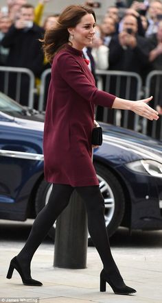 a woman in red coat and black pants walking down the street with her hand out