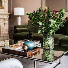 a glass table with flowers and books on it in front of a couch, coffee table