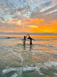 two women are standing in the ocean at sunset with their arms around each other as they hold hands