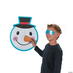 a young boy is holding up a paper snowman cutout with sunglasses on his face