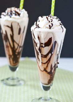 two glasses filled with ice cream and chocolate on top of a green tablecloth next to each other