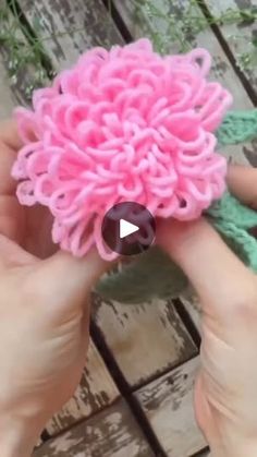 someone is holding a pink flower made out of yarn