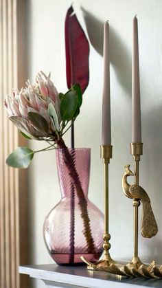 three candles are sitting on a table next to a pink vase with flowers in it